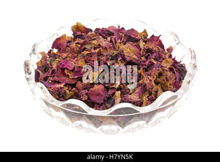 A glass bowl of dried red rosebuds and petals that have been crushed isolated on a white background. Stock Photo