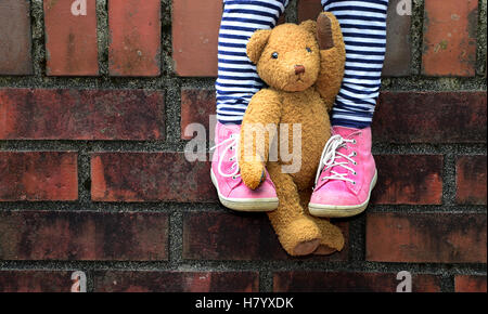 Teddy clamped between legs, child sitting on wall, detail, Germany Stock Photo