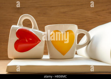 Two cups on book with red and yellow heart-shaped ,on wooden table,focused on cups Stock Photo