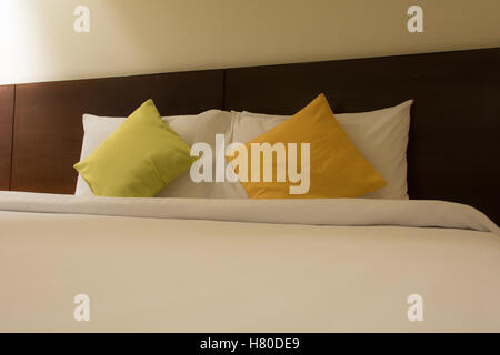 Low key Image of comfortable pillows on the bed with light from the lamp beside the bed at the hotel Stock Photo