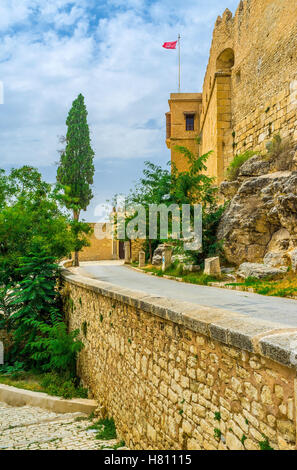 The narrow way among the stone walls and greenery leads to the Kasbah of El Kef, Tunisia. Stock Photo