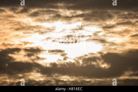 Silhouette plane flying over sunlight on cloudy sky in orange tone color. Stock Photo