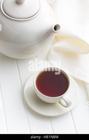 A cup of black tea and teapot on white table. Stock Photo