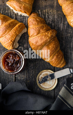 Tasty buttery croissant and jam in jar on old wooden table. Stock Photo