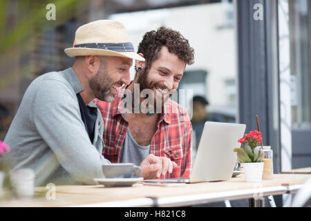 Gay couple sat sharing laptop in cafe