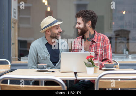 Gay couple sat sharing laptop in cafe
