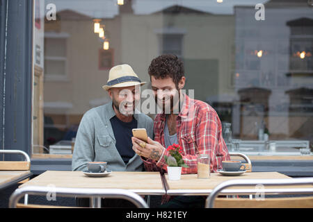 Gay couple sat sharing phone in cafe