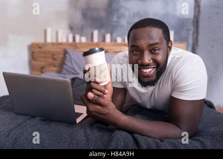Joyful man holding cup of coffee in bedroom Stock Photo