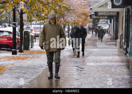 Ilkley, West Yorkshire, UK. 9th November 2016. It is snowing and a man (along with other pedestrians wearing boots, gloves, hats and winter coats) is walking past shops on The Grove - Ilkley's first snowfall of 2016. Credit:  Ian Lamond/Alamy Live News Stock Photo