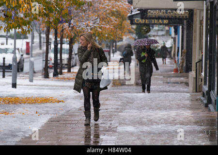 Ilkley, West Yorkshire, UK. 9th November 2016. It is snowing and pedestrians (wearing boots, winter coats and holding umbrellas) are walking past shops on The Grove - Ilkley's first snowfall of 2016. Credit:  Ian Lamond/Alamy Live News Stock Photo