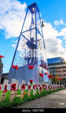 Glasgow, Scotland, UK. 10th November, 2016. In preparation for the Remembrance Services on 11 November the statue of 'Every Man Remembered' by MARK HUMPHREY, a 23 foot high brass statue of the Unknown Soldier enclosed in glass and with 100's of poppies floating in the case, is adorned by Remembrance Crosses and Solitary Poppies by members of the public and Poppy Scotland. The statue can be seen at the Remembrance Garden, George Square, Glasgow city centre. Credit:  Findlay/Alamy Live News Stock Photo