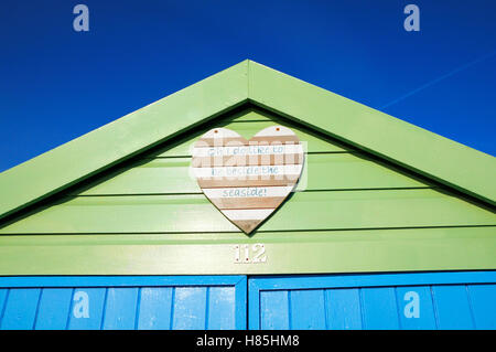 Freshly painted beach hut with a cheery wooden heart plaque displaying the lyrics "Oh I do like to be beside the seaside!" Stock Photo