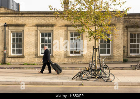 A man walks past the Railway Station in Cambridge UK at the new Station Plaza, pulling a wheeled suitcase Stock Photo