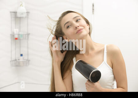 Beautiful young woman looking at the mirror drying hair Stock Photo