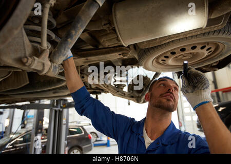 mechanic man with flashlight repairing car at shop Stock Photo