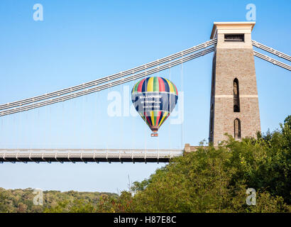 A hot air balloon dropping behind the Clifton suspension bridge in Bristol UK during an early morning flight Stock Photo