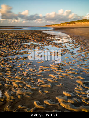 Süderdünen, Langeoog.  Deutschland.  Germany.  A view along the beech at low tide in the golden hour.  The soft warm sunshine reflects on the water in the shallow pools-of-water that remain in the deep patterns in the sun.  The long exposure causes movement blur in the fast moving clouds. Stock Photo