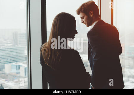 Group of business people, a man in a formal suit and a woman in a jacket, standing near the window, winter city landscape Stock Photo