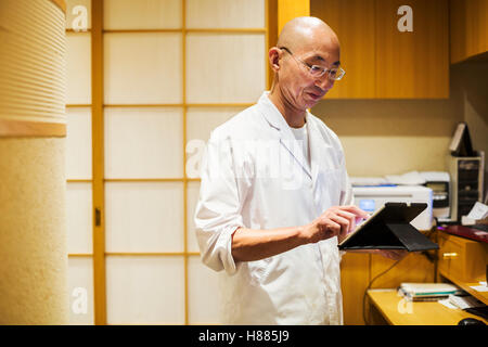 A chef in a small commercial kitchen, an itamae or master chef using a digital tablet. Stock Photo