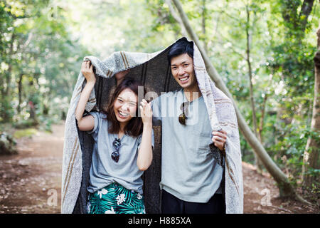 Young woman and man standing in a forest, holding a blanket over their heads. Stock Photo
