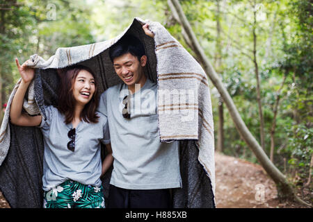 Young woman and man standing in a forest, holding a blanket over their heads. Stock Photo