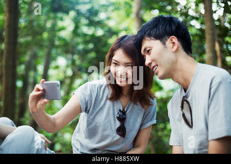 Young woman and a man sitting in a forest, taking a selfie. Stock Photo