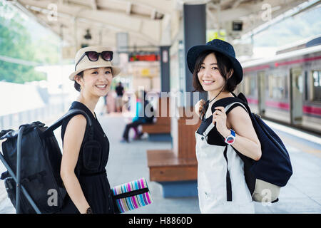 Two young women standing on a platform at a railway station.