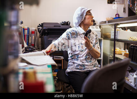 A mature woman at a desk in the office of a noodle production factory on the telephone. Stock Photo