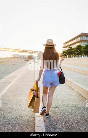 Young woman with long brown hair, wearing Panama hat and carrying shopping bags. Stock Photo