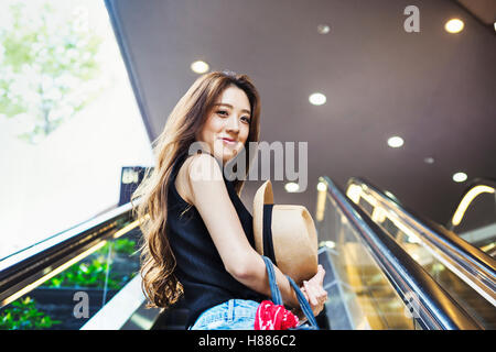 Smiling young woman with long brown hair on an escalator. Stock Photo