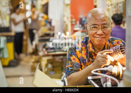 A senior craftsman in a glass maker's workshop using a light to check an etched or cut glass pattern. Stock Photo