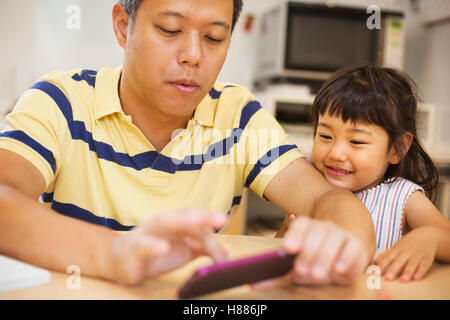 Family home. A man using a smart phone, his daughter beside him. Stock Photo