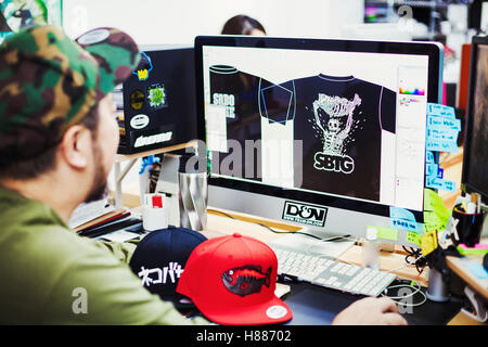 Design Studio. A man seated at a desk using a computer to design tee shirt prints. Stock Photo