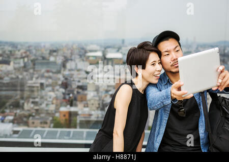 Two people, man and woman taking a selfie with a digital tablet, in front of a view over a large city. Stock Photo