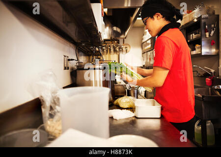 The ramen noodle shop. A chef working in a kitchen preparing food using a stove and large pans. Stock Photo