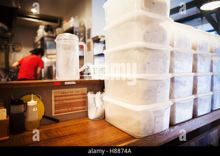 The ramen noodle shop.  Staff preparing food in a kitchen, and rows of plastic boxes of food. Stock Photo