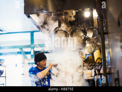 The ramen noodle shop. A chef working in a kitchen with steam rising from the pots of noodles. Stock Photo