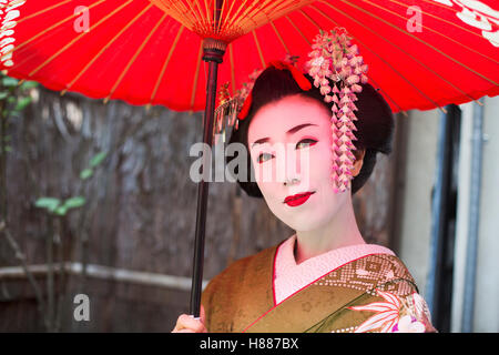 A woman dressed in the traditional geisha style, wearing a kimono with an elaborate hairstyle, holding a parasol Stock Photo
