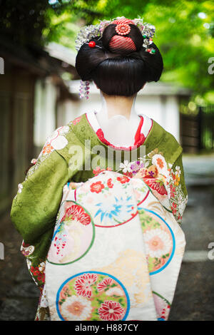 A woman dressed in the traditional geisha style, wearing a kimono and obi, on a street. Stock Photo