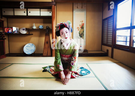 A woman dressed in the traditional geisha style, wearing a kimono and obi, kneeling in a traditional pose.