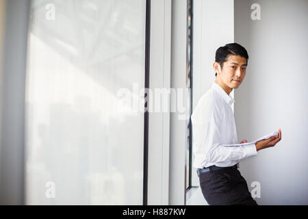 A businessman in the office, by a large window, using his smart phone. Stock Photo