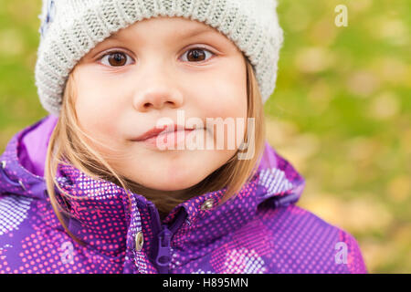 Funny smiling Caucasian little girl, close-up outdoor portrait, walking in autumnal park Stock Photo