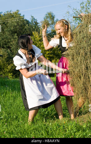 Two young woman wearing Dirndl dresses harvesting hay Stock Photo