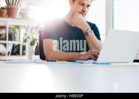 Indoor shot of young man sitting at a table and working on laptop. Business man using laptop computer while sitting at his desk Stock Photo