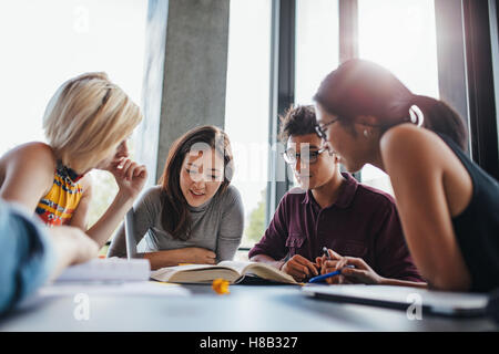 university students in cooperation with their assignment at library. Group of young people sitting at table reading books. Stock Photo