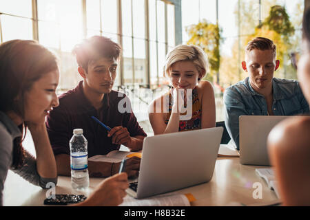 university friends socializing and studying together. Group of students sitting at table in library and using laptop. Stock Photo