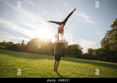 Fit young couple doing acro yoga in park. Man holding and balancing woman in air. Stock Photo