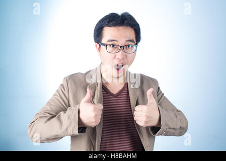 Asian guy making, showing thumbs up with a Smiling, on blue background Stock Photo