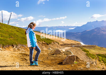 Girl with a pigtail, dressed in sports jacket and warm fluffy headphones, admires of autumn mountain landscape, Sochi, Russia Stock Photo