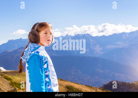 Girl with a pigtail, dressed in sports jacket and warm fluffy headphones, admires of autumn mountain landscape, Sochi, Russia Stock Photo